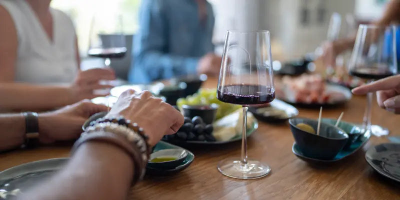 Ein festlich gedeckter Tisch mit einer Auswahl an köstlichem Fingerfood und mehreren Gläsern, gefüllt mit Rotwein. Die stilvolle Anordnung lädt zu einem genussvollen Wein-Tasting in geselliger Atmosphäre ein.